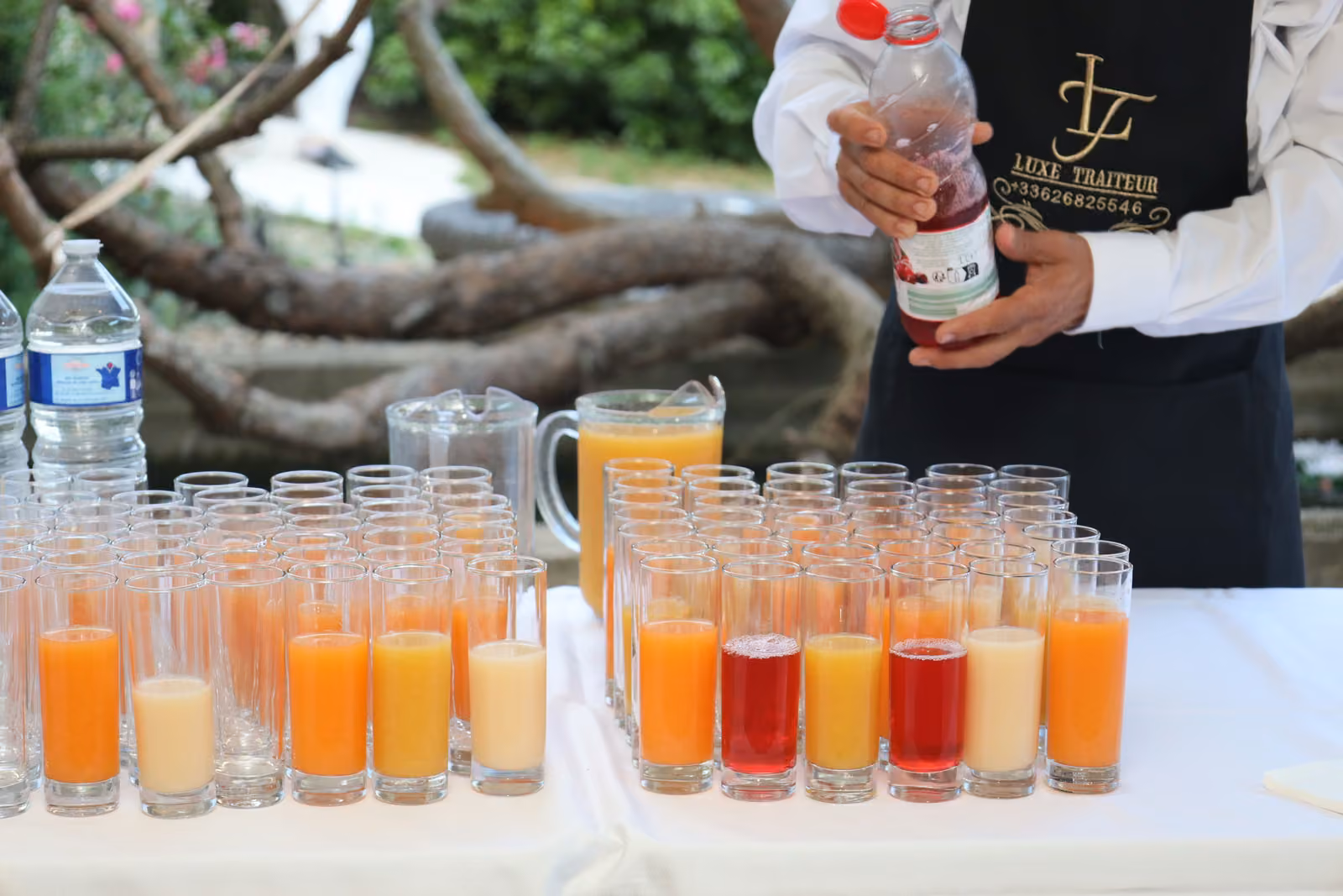 Bar à jus et cocktails sans alcool Serveur en tablier noir versant des jus et cocktails sans alcool dans des verres alignés sur un buffet