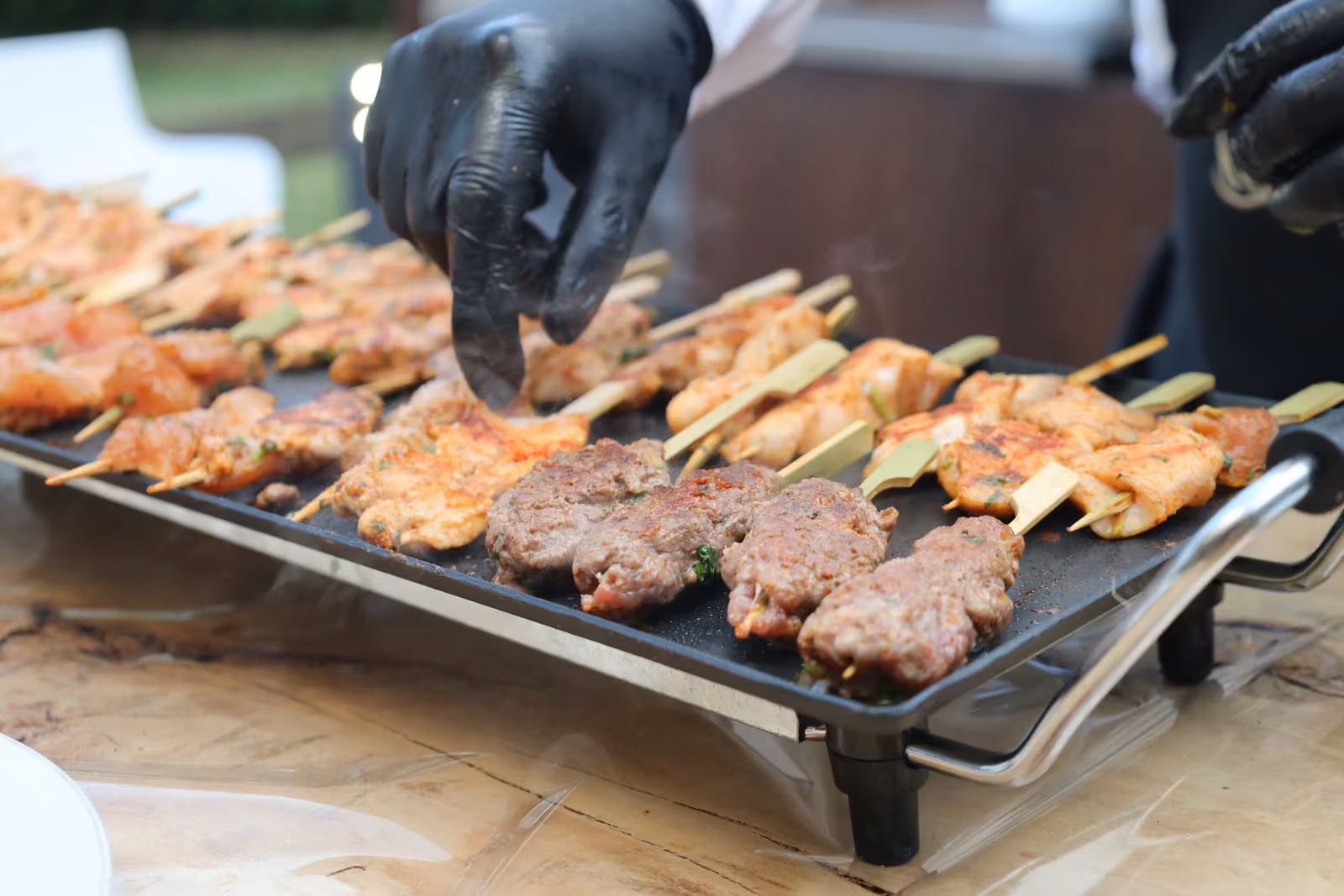 Brochettes de poulet et kefta à la plancha Main gantée retournant des brochettes de poulet et de kefta sur une plancha