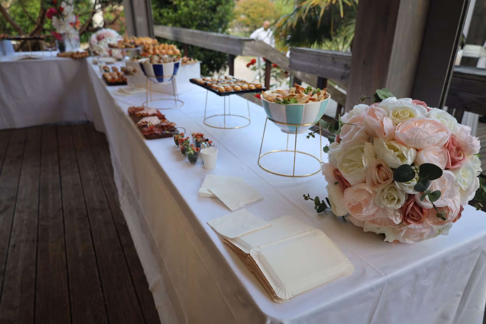 Buffet et bouquet de roses Long buffet nappé de blanc en terrasse, bouquet de roses blanches et roses au premier plan