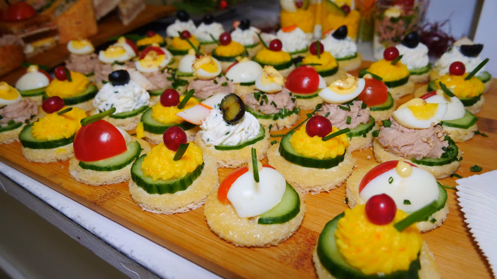 Canapés variés Canapés variés sur un plateau en bois : œuf, thon, tomate cerise, concombre et olive