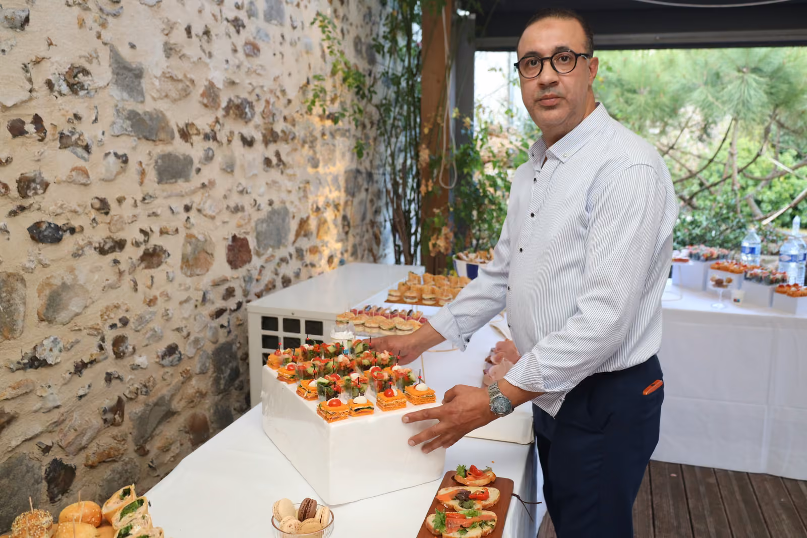 Dressage des canapés par le chef Chef traiteur en chemise blanche dressant des canapés sur un présentoir, devant un mur en pierre