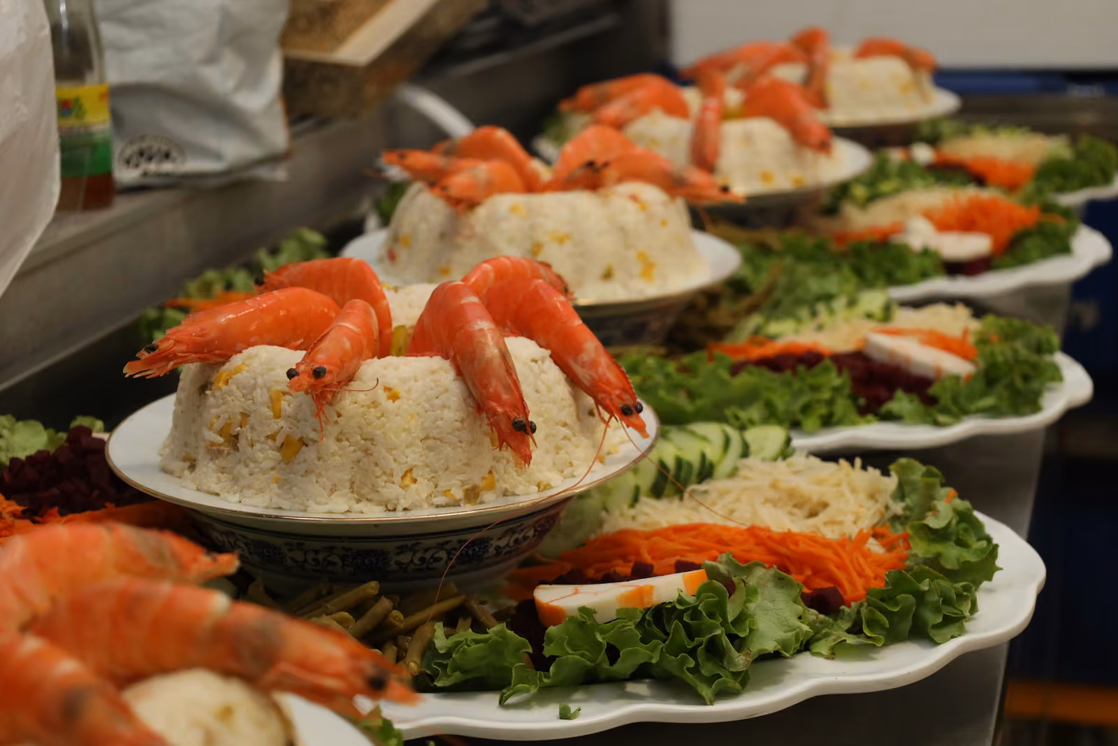 Couronnes de riz aux crevettes Couronnes de riz garnies de crevettes entières sur lit de salade et crudités, alignées en cuisine