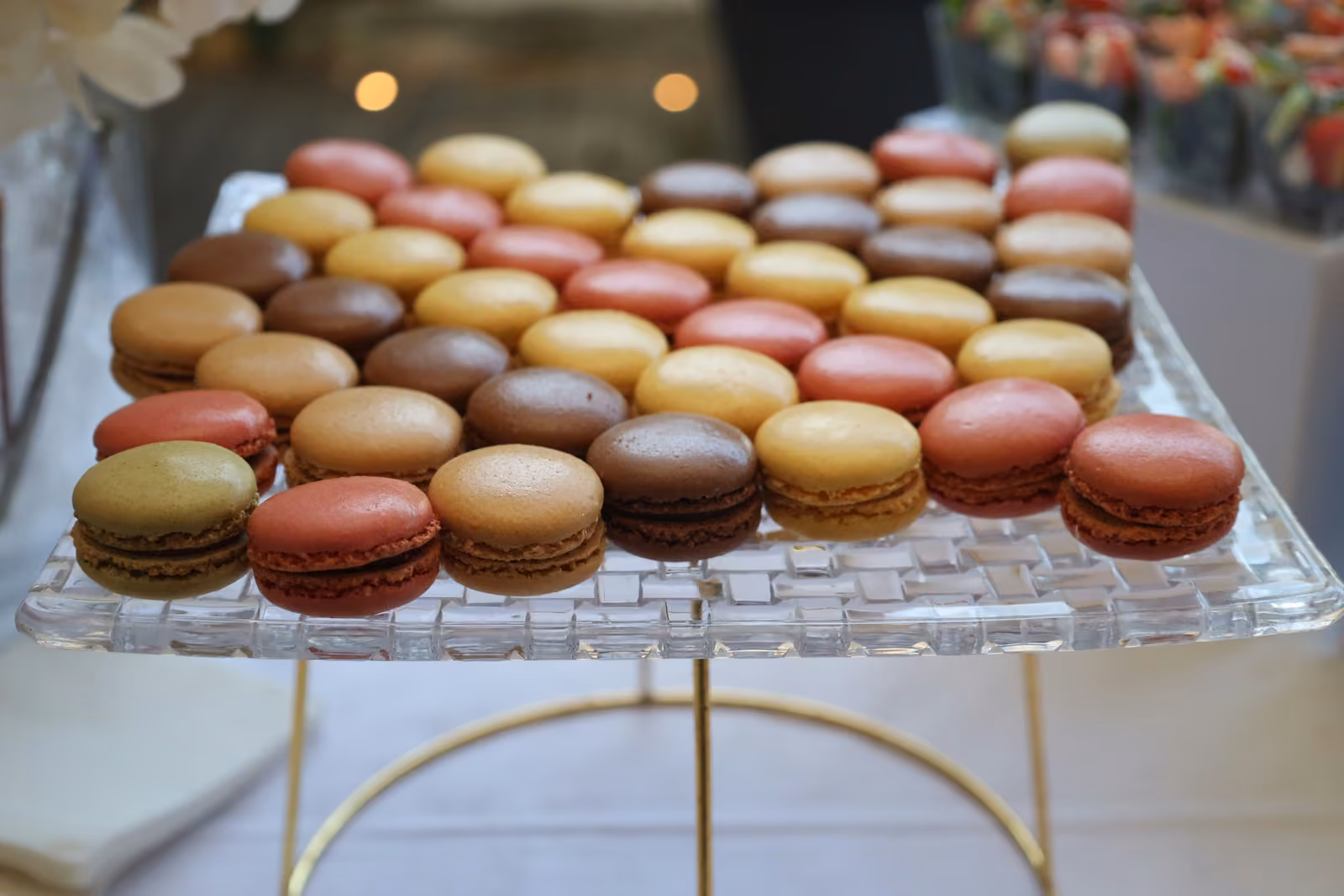 Macarons assortis alignés sur un plateau en verre : pistache, chocolat, framboise, vanille