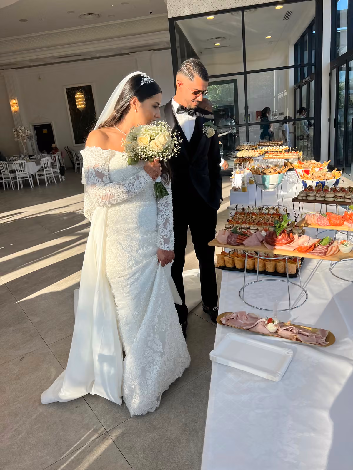 Les mariés devant le buffet Mariés en robe blanche et costume noir découvrant le buffet du traiteur