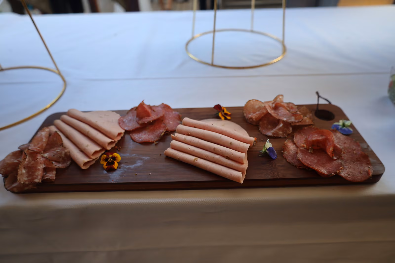 Planche de charcuterie Planche en bois de charcuterie : jambon blanc, saucisson et rosette, fleurs comestibles