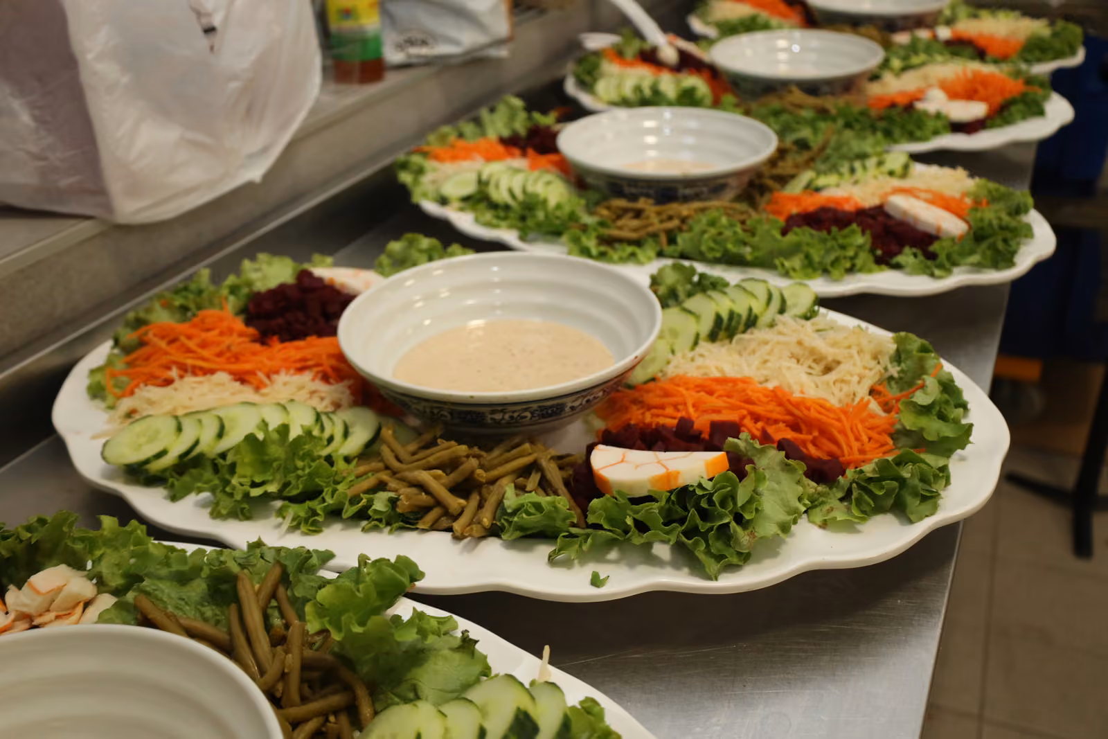 Plats de crudités en préparation Grands plats de crudités, carottes râpées, betteraves et sauce préparés en cuisine avant le service