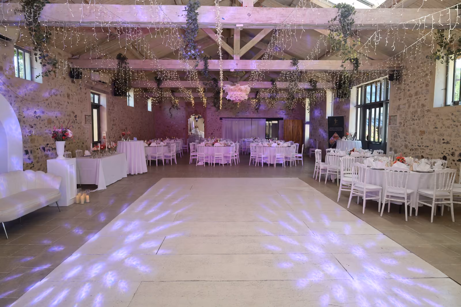 Salle de réception de mariage et piste de danse Salle de réception de mariage en pierre et poutres apparentes, piste de danse blanche et tables dressées