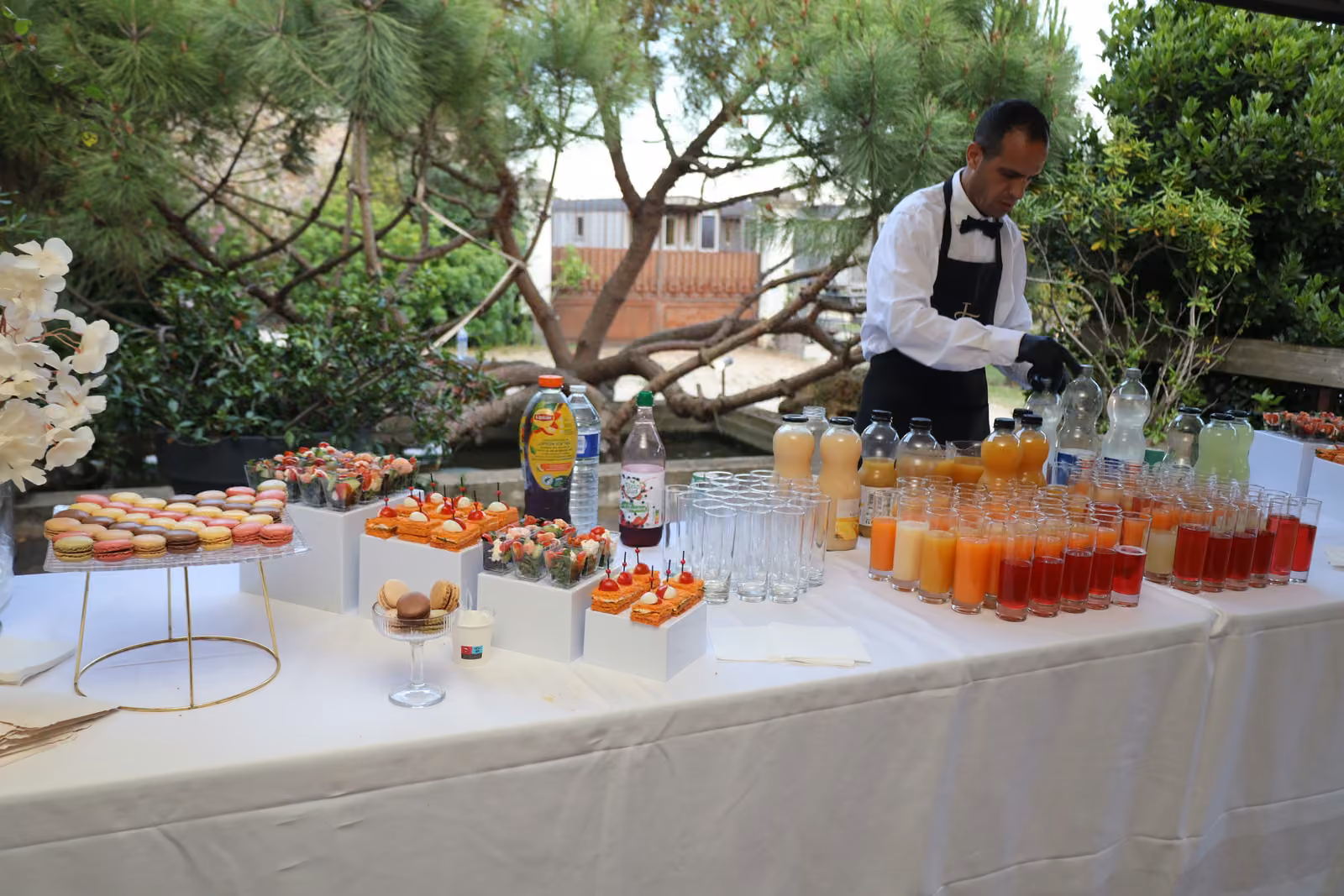 Service au bar à jus Serveur en nœud papillon préparant des jus frais au bout d'un buffet installé en jardin